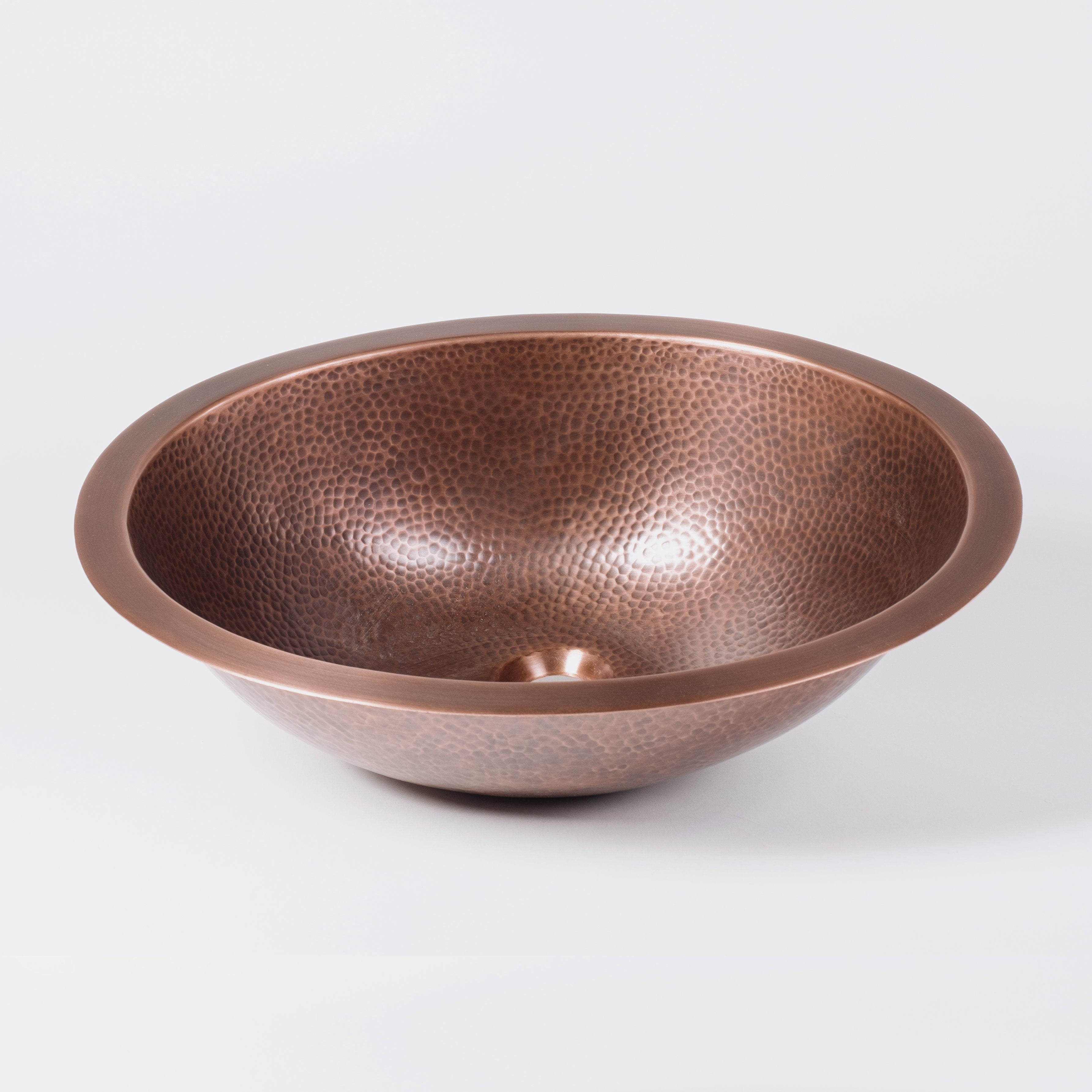 An oval-shaped, hammered copper sink with a patinated finish.