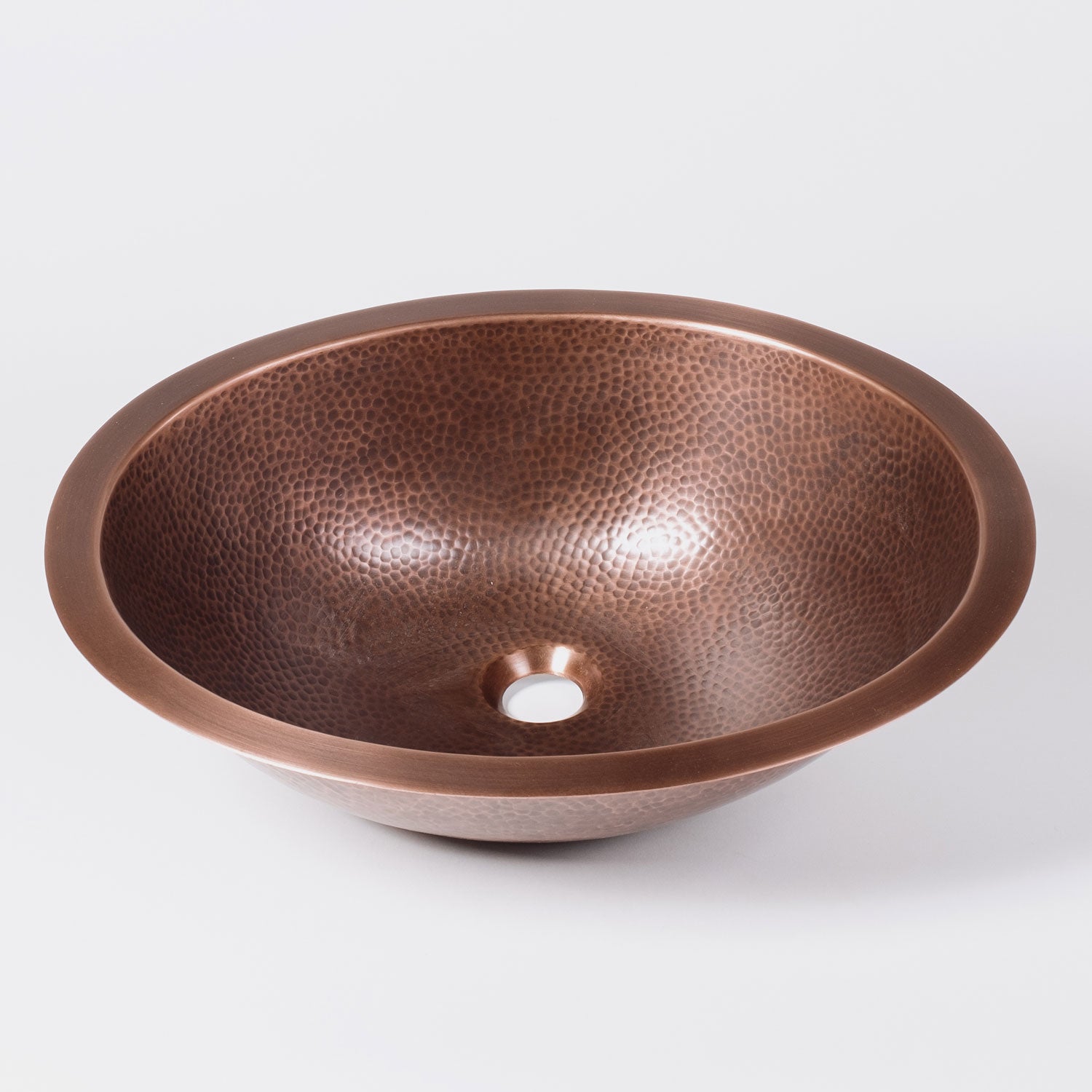 An oval-shaped, hammered copper sink with a patinated finish.
