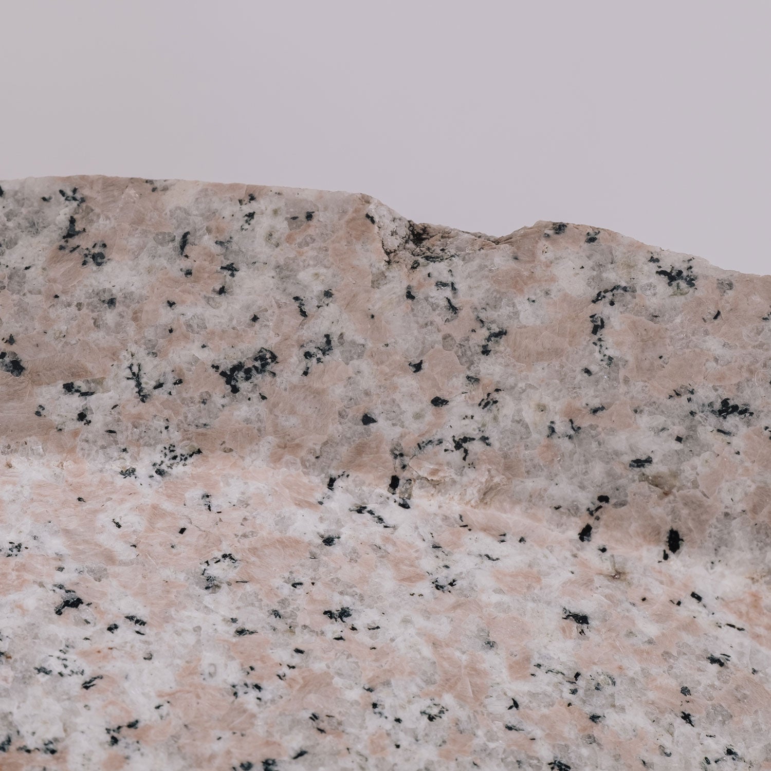 A round vessel sink made of rose granite with a rough, chiseled texture on the exterior and a polished interior and rim. detail