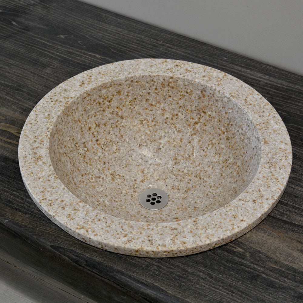 A beige granite self-rimming sink is placed on a wooden countertop with a dark granite backdrop.
