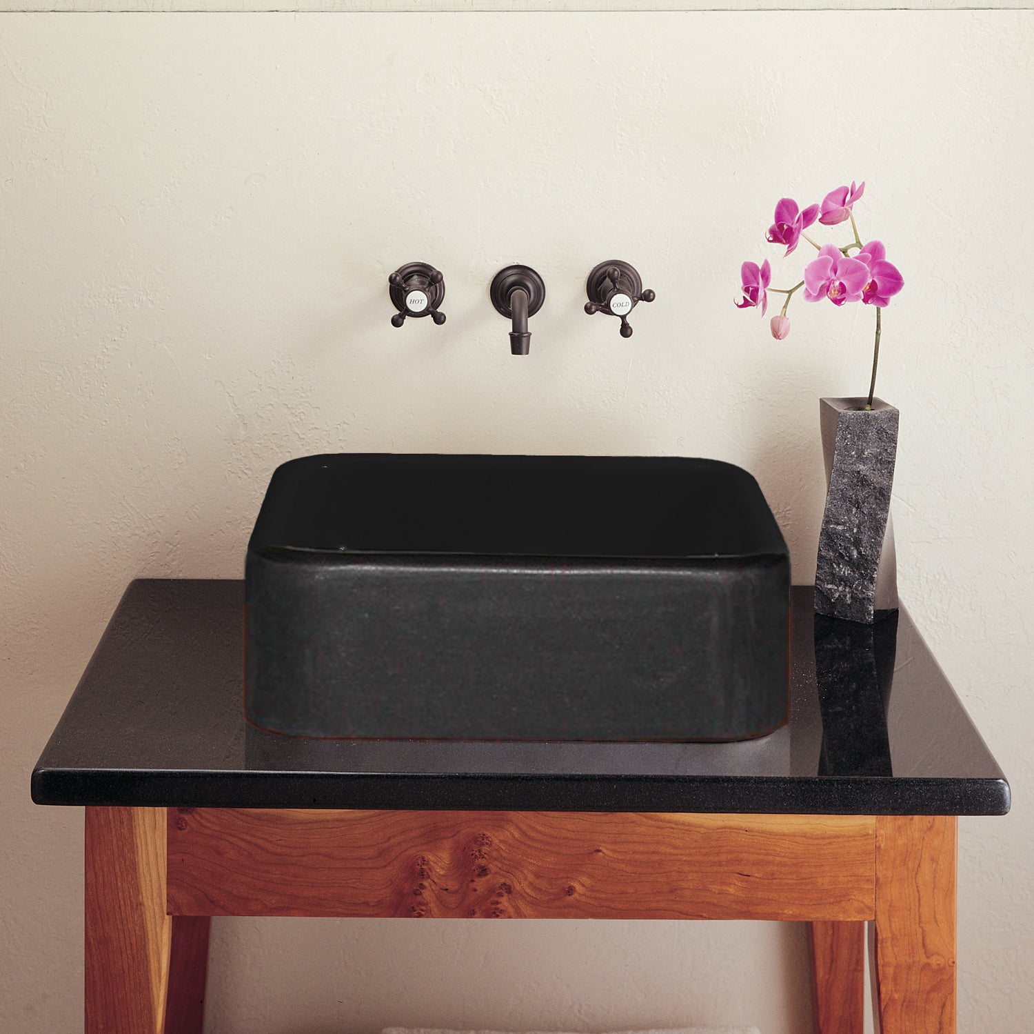 Black sink on a wooden vanity with pink flowers in the background