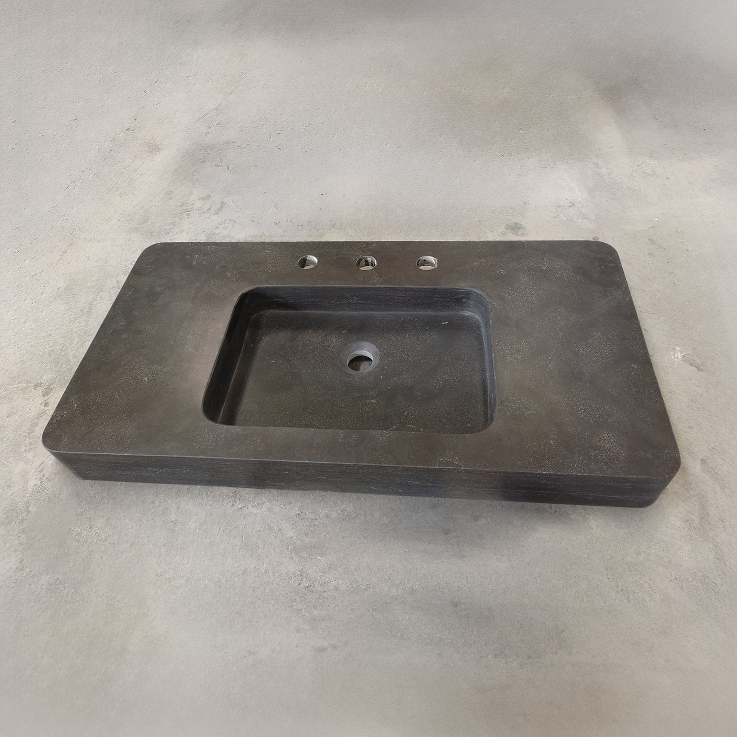 An antique gray limestone sink with a rectangular shape, featuring a central integral sink and sitting on a plain surface.