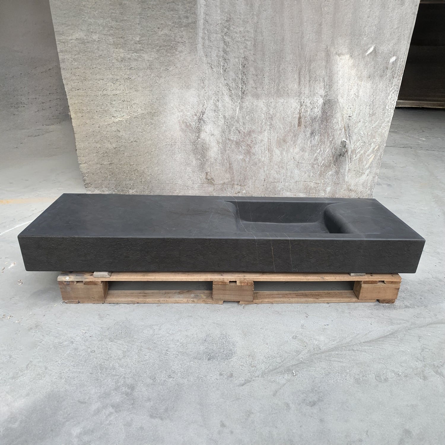 A rectangular, dark gray custom integral sink placed on a wooden pallet against a textured gray background.
