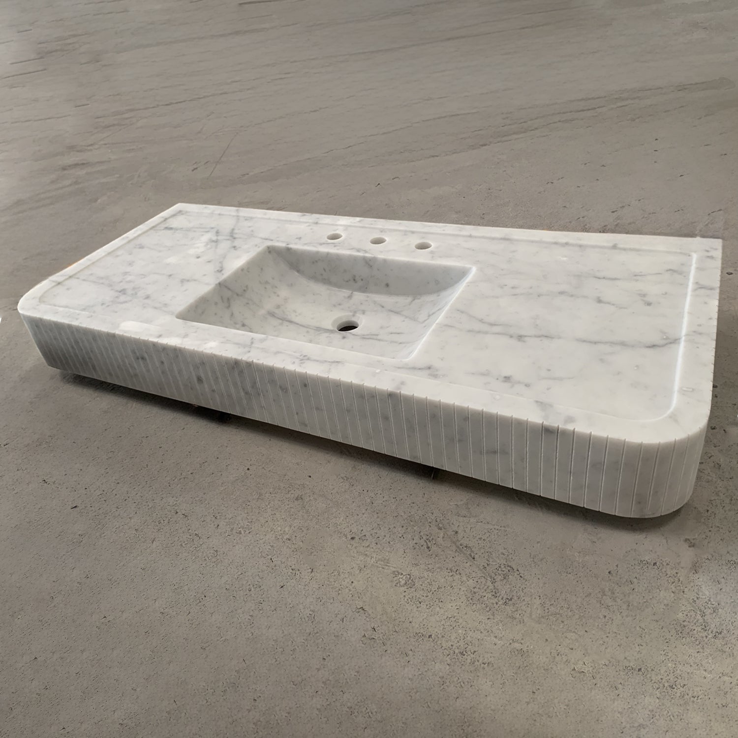 A white marble vanity with a fluted front, featuring an integral sink.