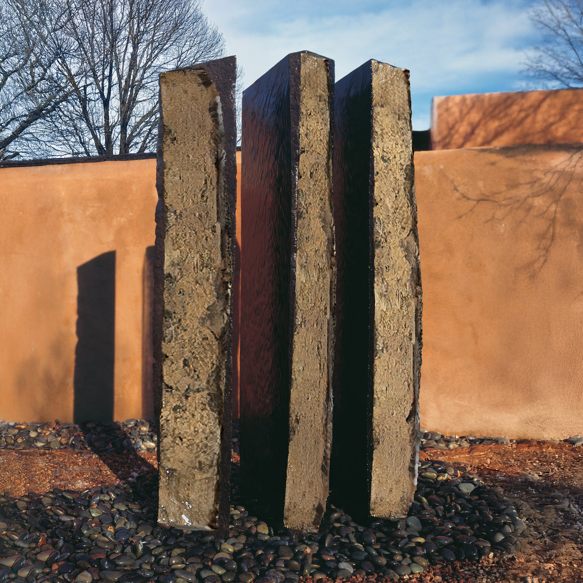A vertical, columnar basalt fountain installed on a bed of pebbles, with natural weathered exterior and mirror polish surfaces. image 4 of 4