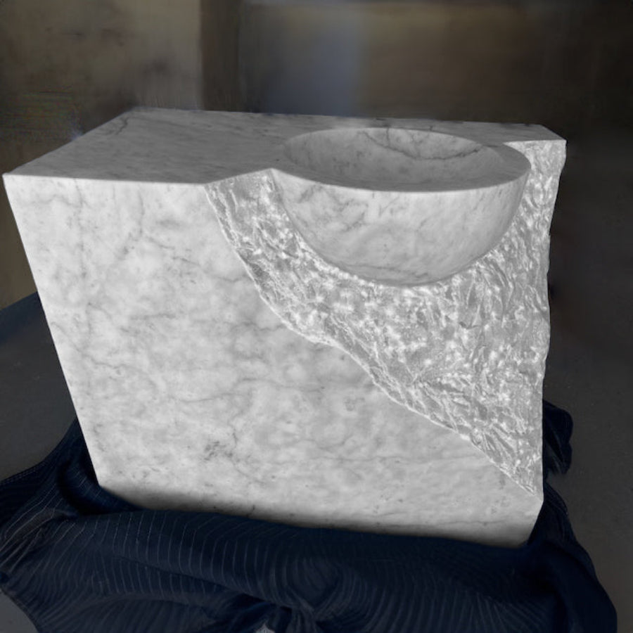 A Carrara marble vanity with a rough chisel design, displayed against a dark, textured background.