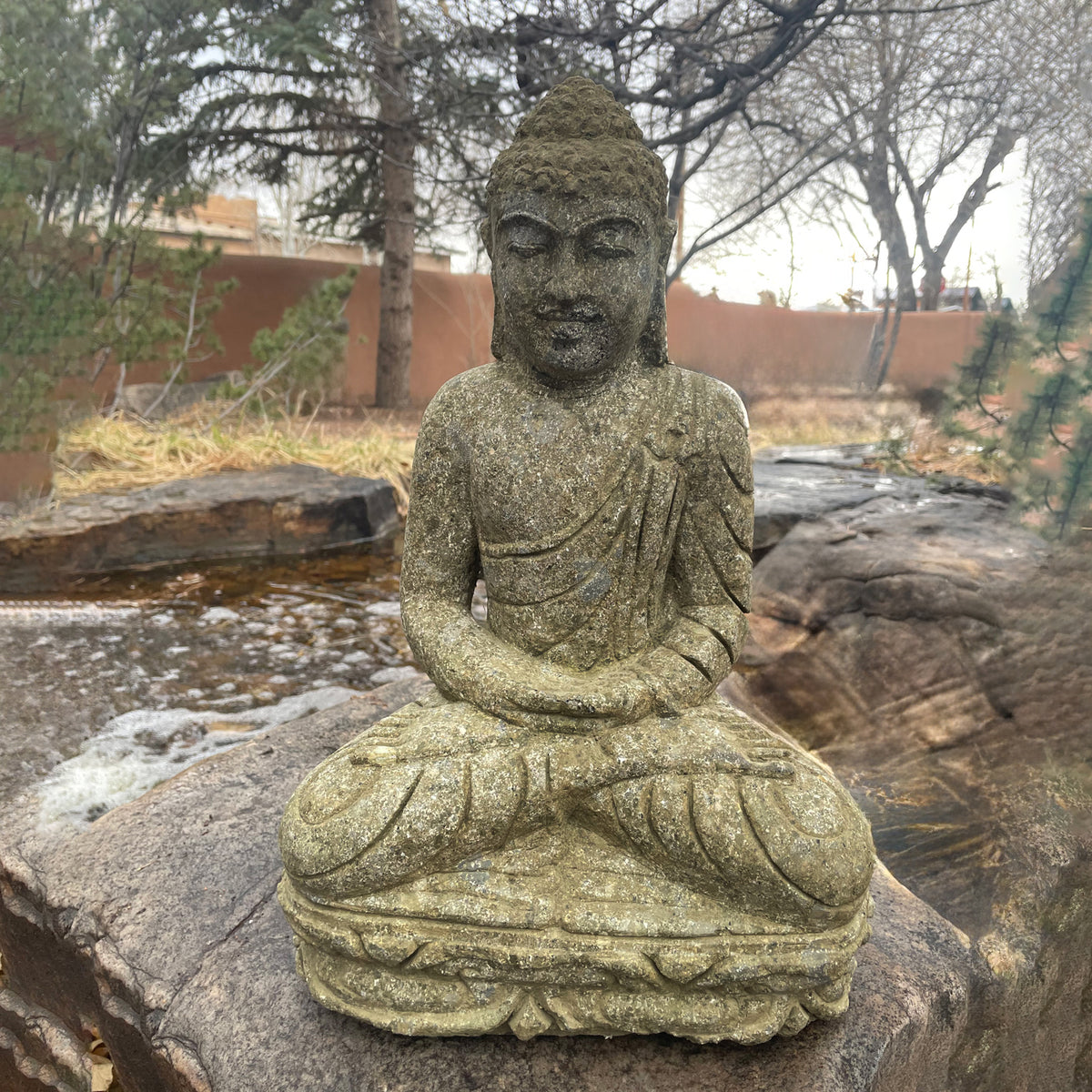 A hand-carved stone Buddha statue, sitting in a meditative pose, made from Verde Basalt, placed on stone. image 4 of 5