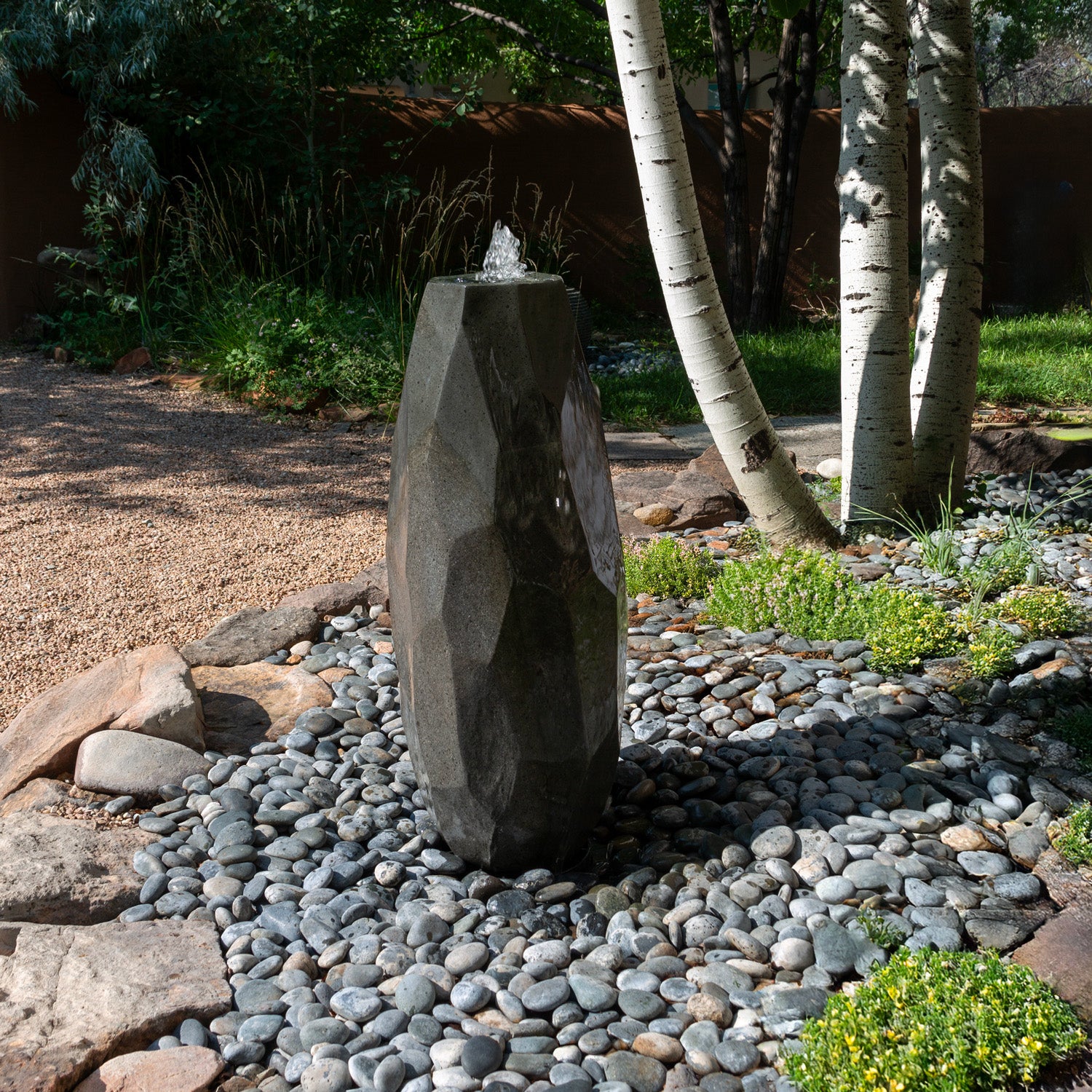 Lithic Fountain, a water feature in a garden setting with pebbles and plants.