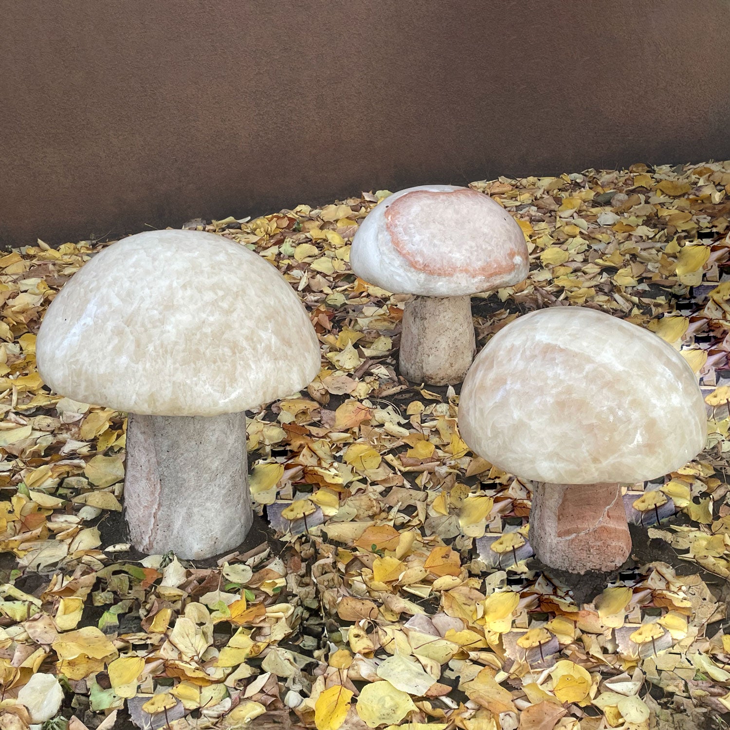 Three garden mushrooms carved from onyx, placed in a garden setting.
