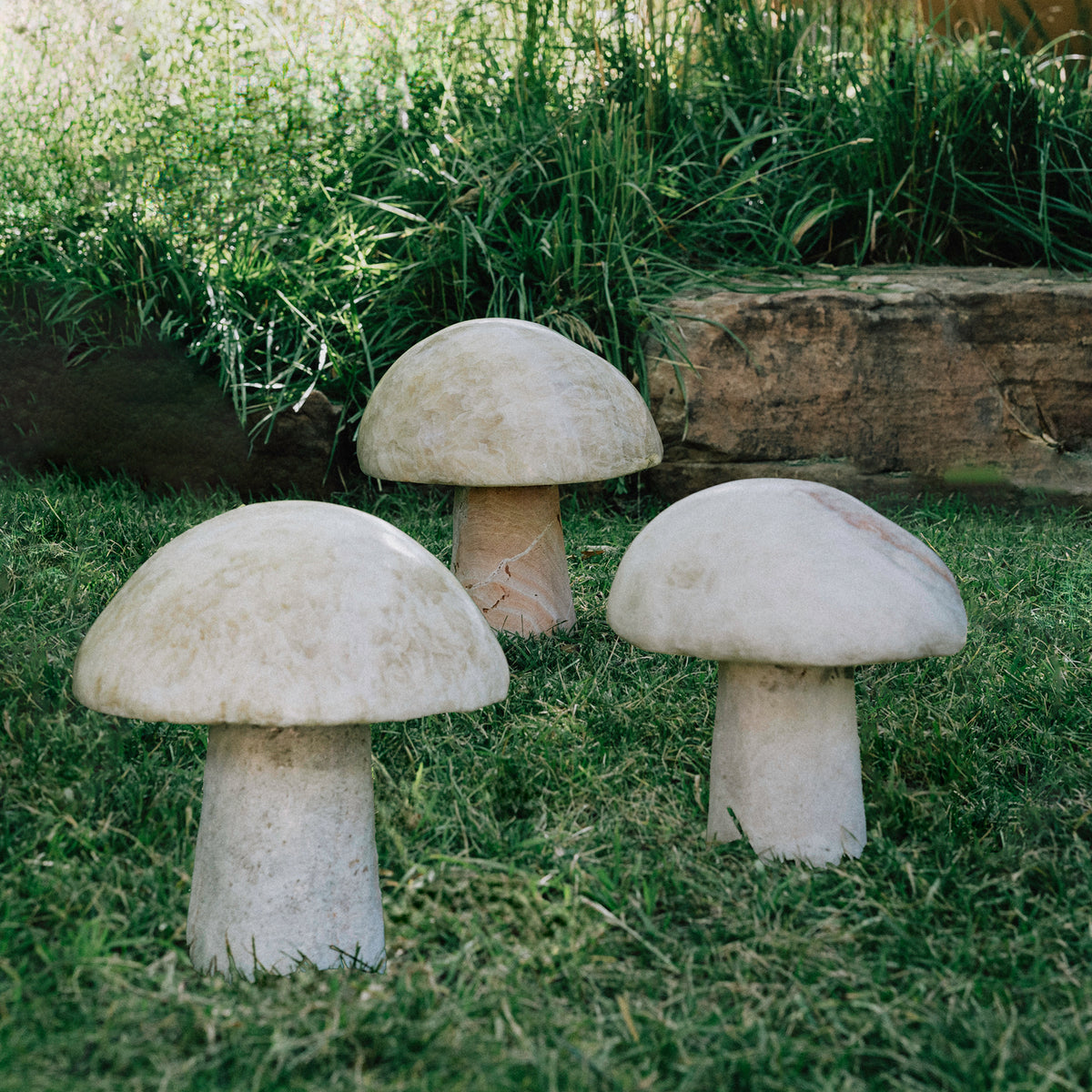 Three garden mushrooms carved from onyx, placed in a garden setting. image 5 of 6