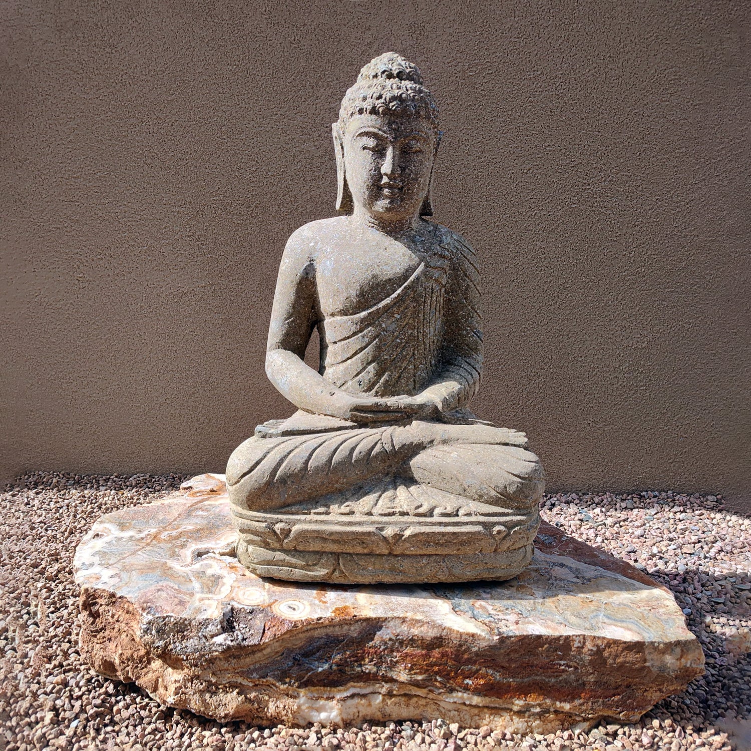 Stone Buddha statue on a rock with a plain background