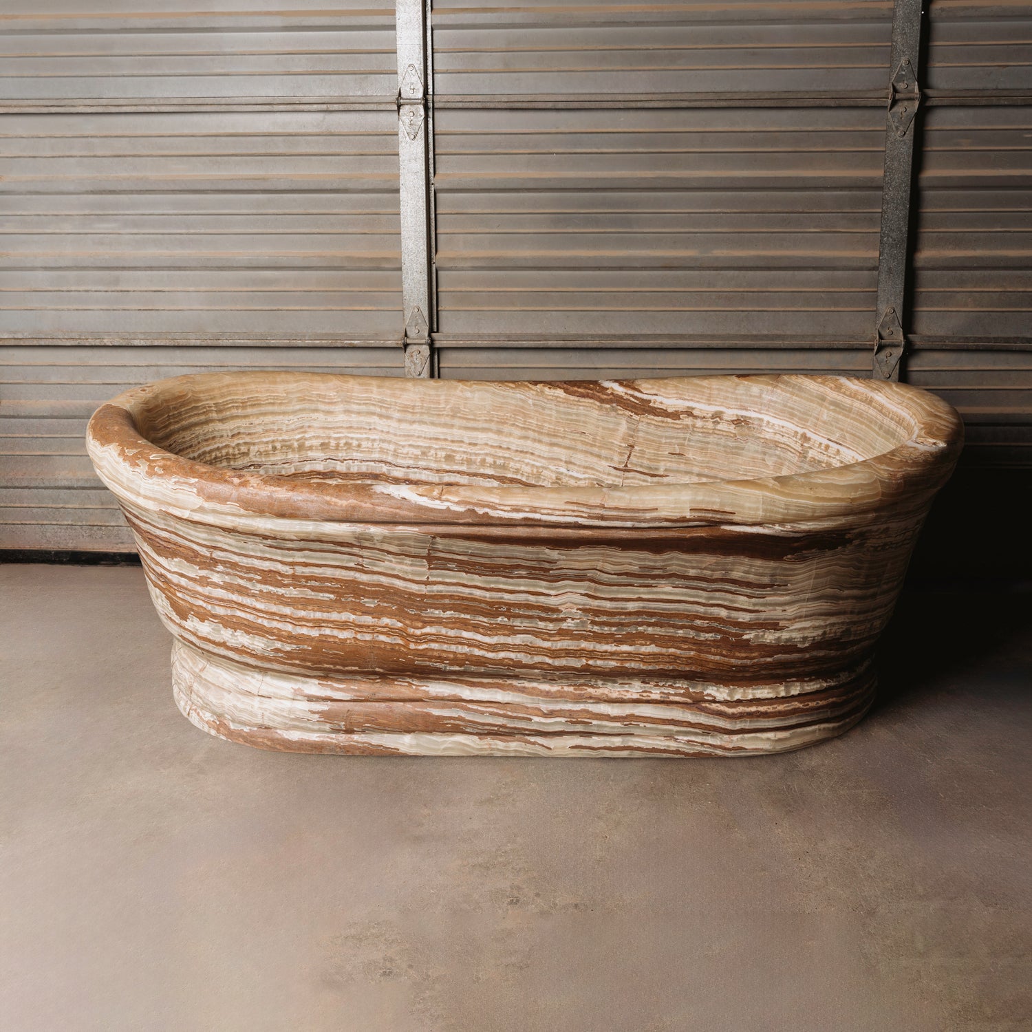 A large, oval-shaped, multi-color onyx planter placed on a concrete floor with wooden vertical elements in the background.