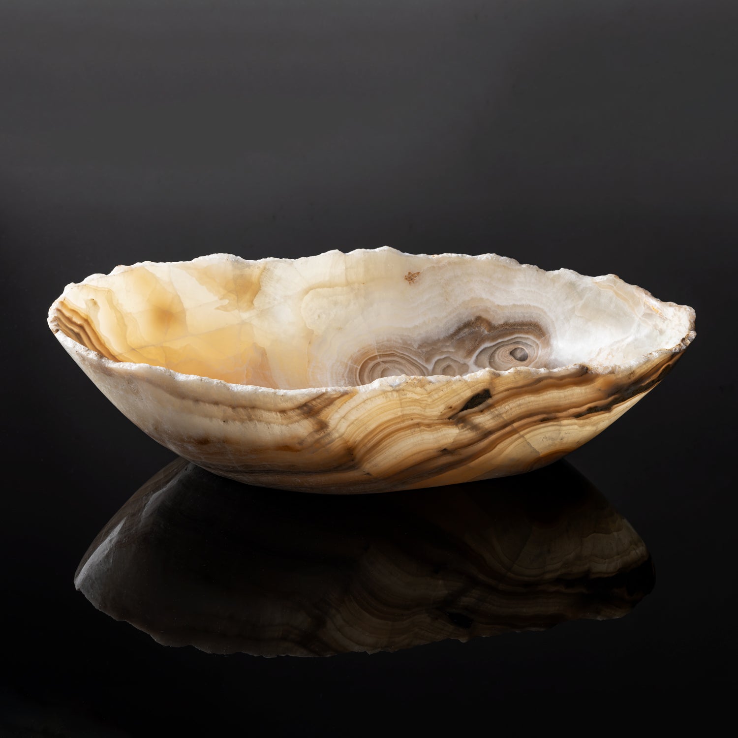 A free form onyx bowl with a smooth, curved shape, displaying swirls of color against a dark background.