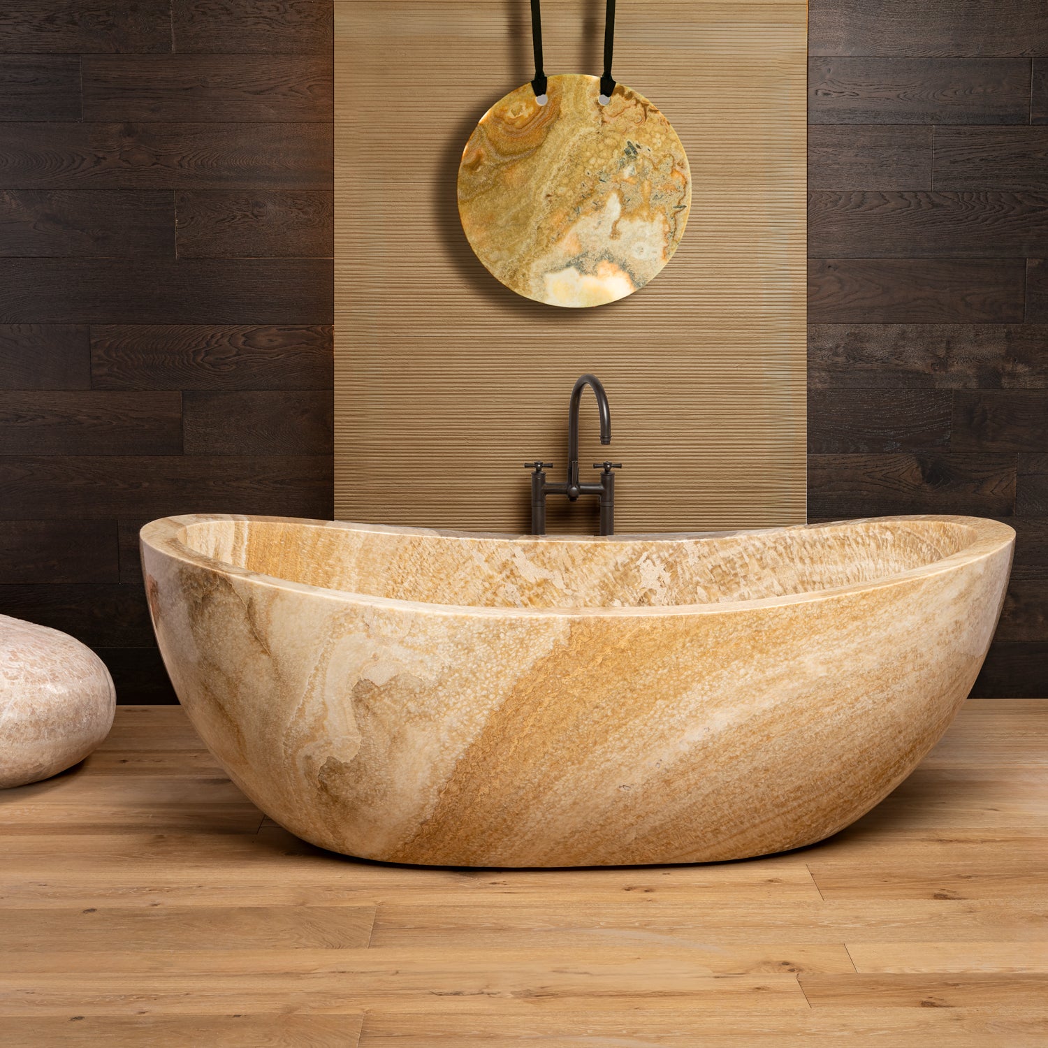 A honey onyx Bateau Bathtub placed on a wooden floor against a wooden wall, with a pendant light hanging above it.