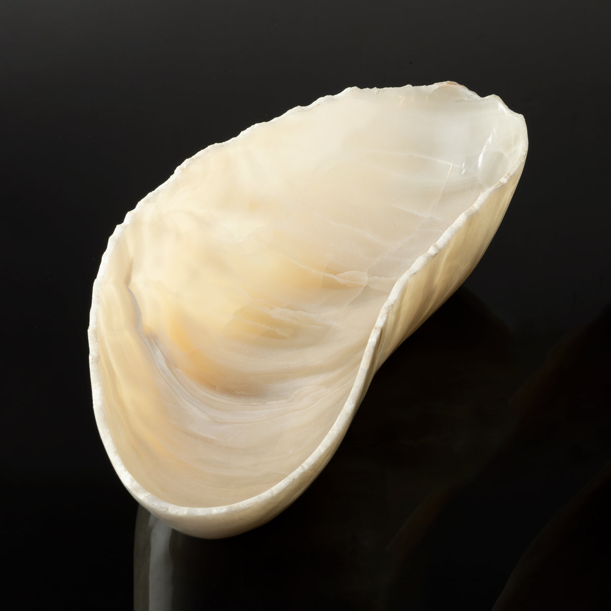 A free form onyx bowl with a smooth, curved shape against a dark background. image 3 of 6
