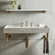 A wall-mounted Ventus bathroom sink carved from carrara marble on an aged brass wall unit.
