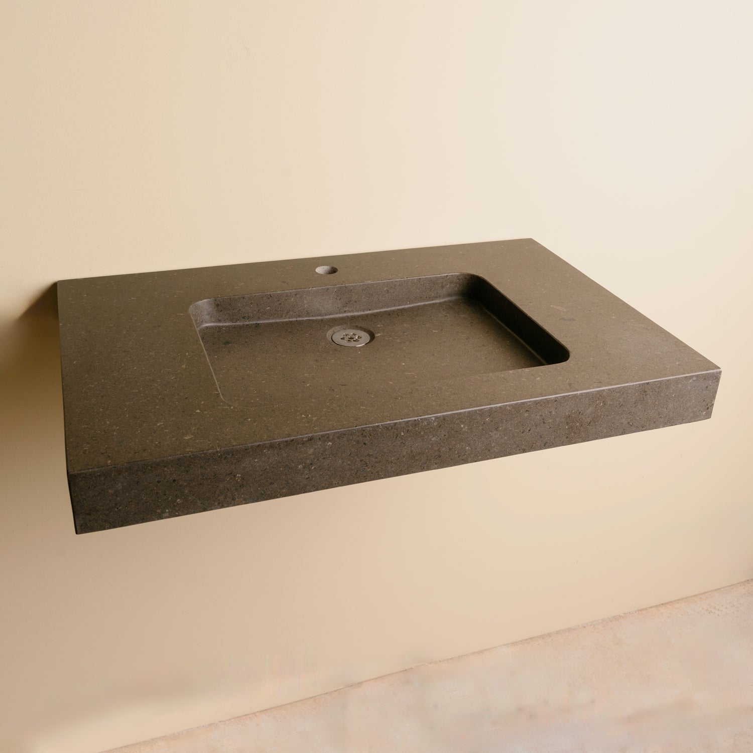 A contemporary bath vanity with an integral sink carved from a solid block of noce basalt. It has a center-hole faucet drilling.