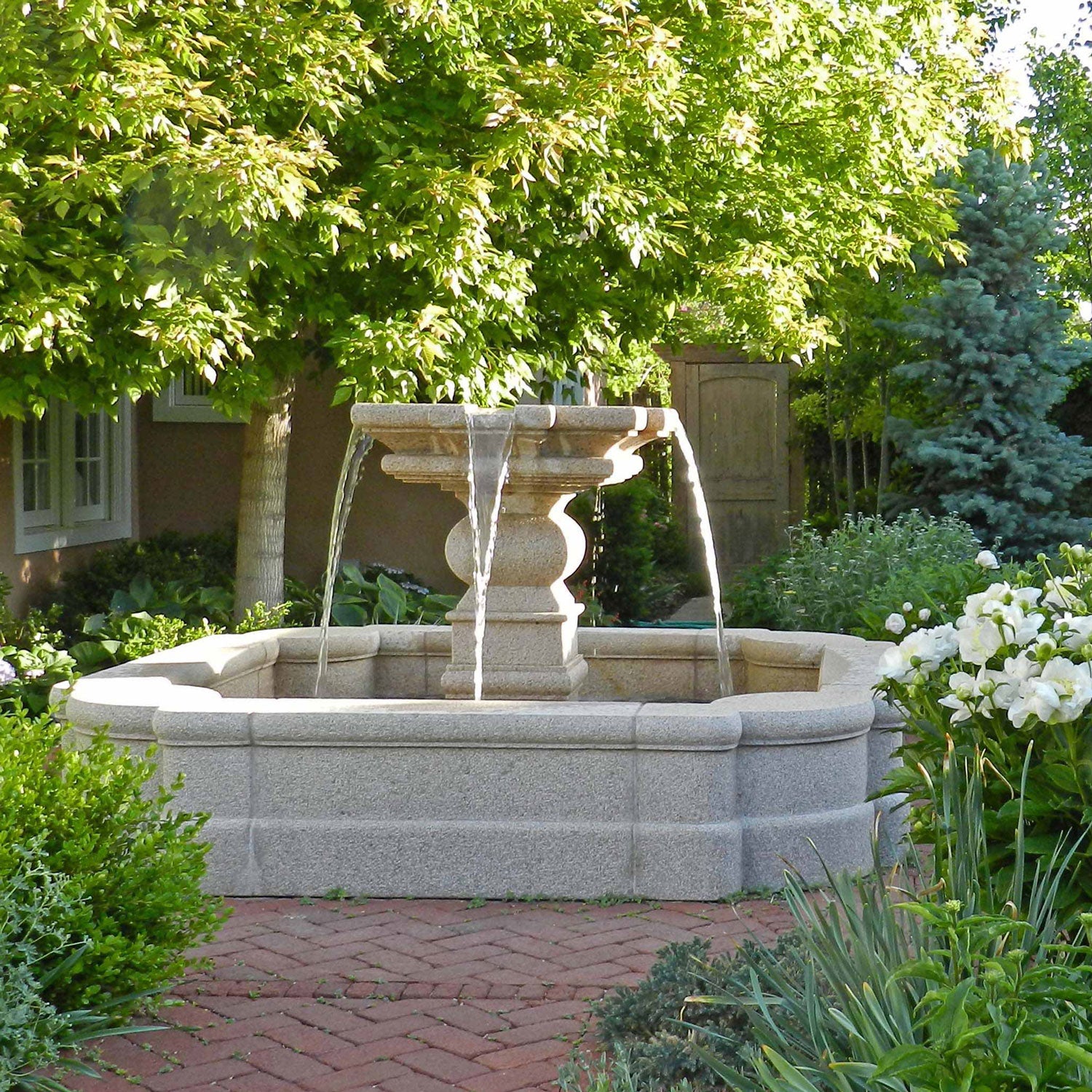 A traditional garden-style fountain made of granite, with water flowing from the top, placed on a brick pathway in a garden setting.