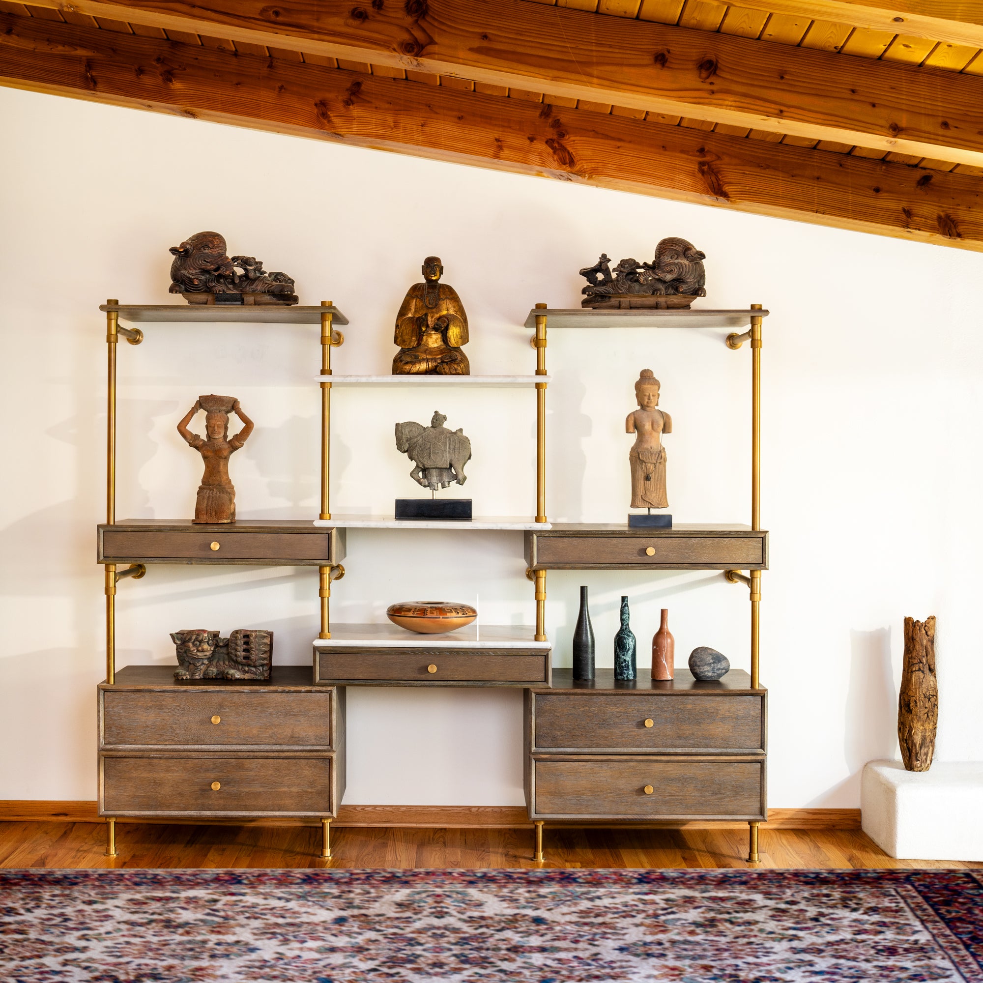 A set of storage drawers and shelves with aged brass legs, cement gray wood, and various decorative items on the shelves.