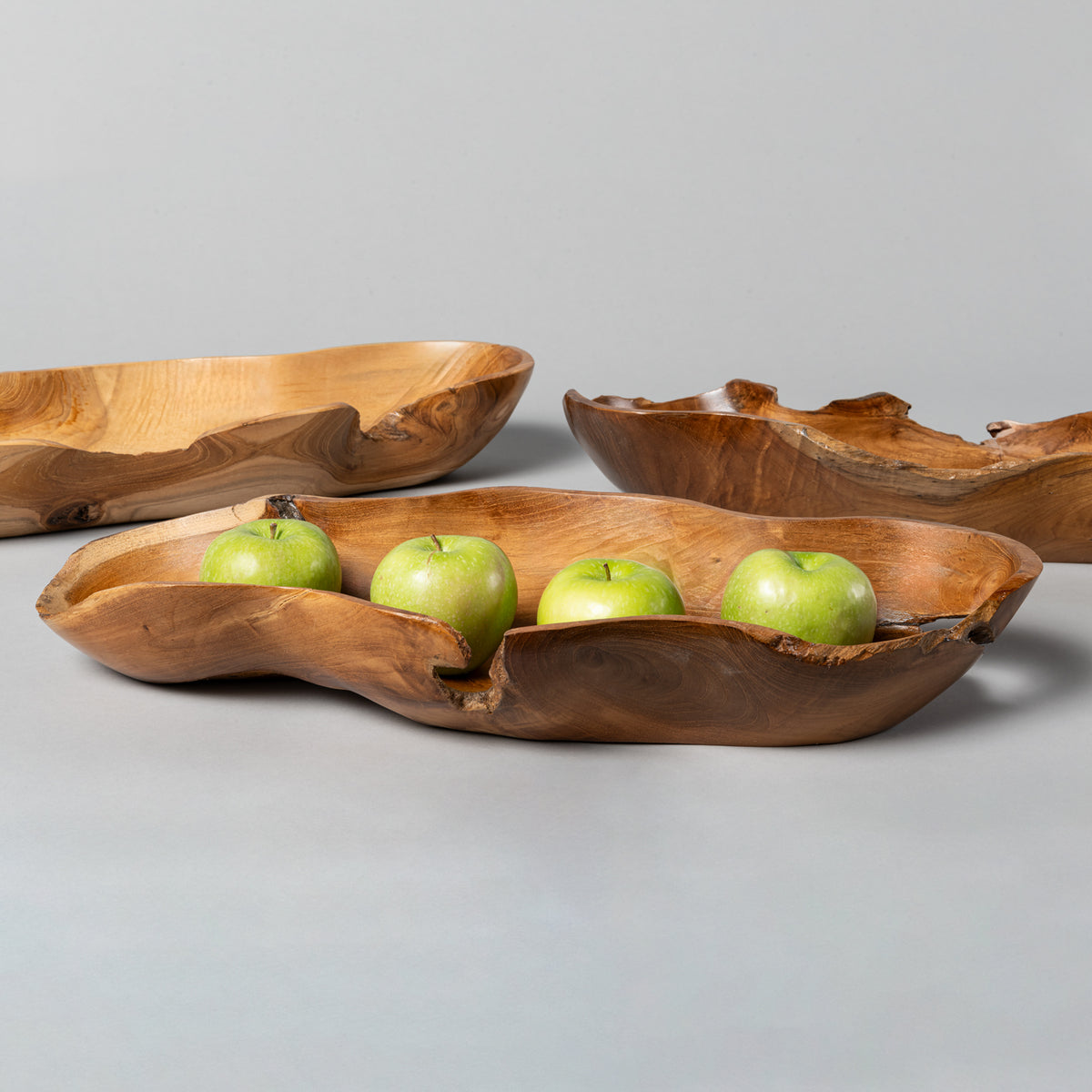 A set of three hand-carved wooden bowls of varying sizes, with the largest bowl containing three green apples. image 2 of 6