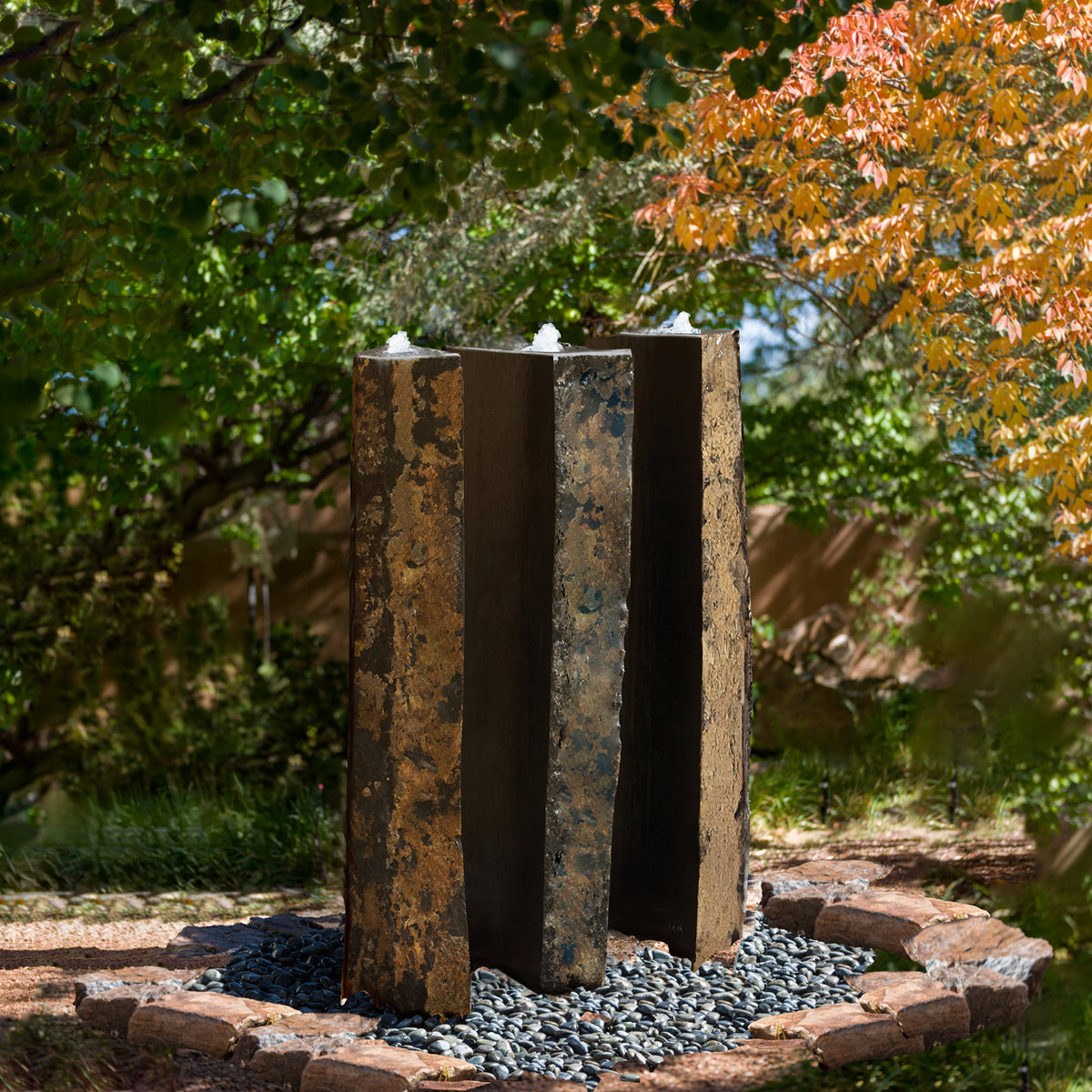 A vertical, columnar basalt fountain installed on a bed of pebbles, with natural weathered exterior and mirror polish surfaces. image 3 of 4