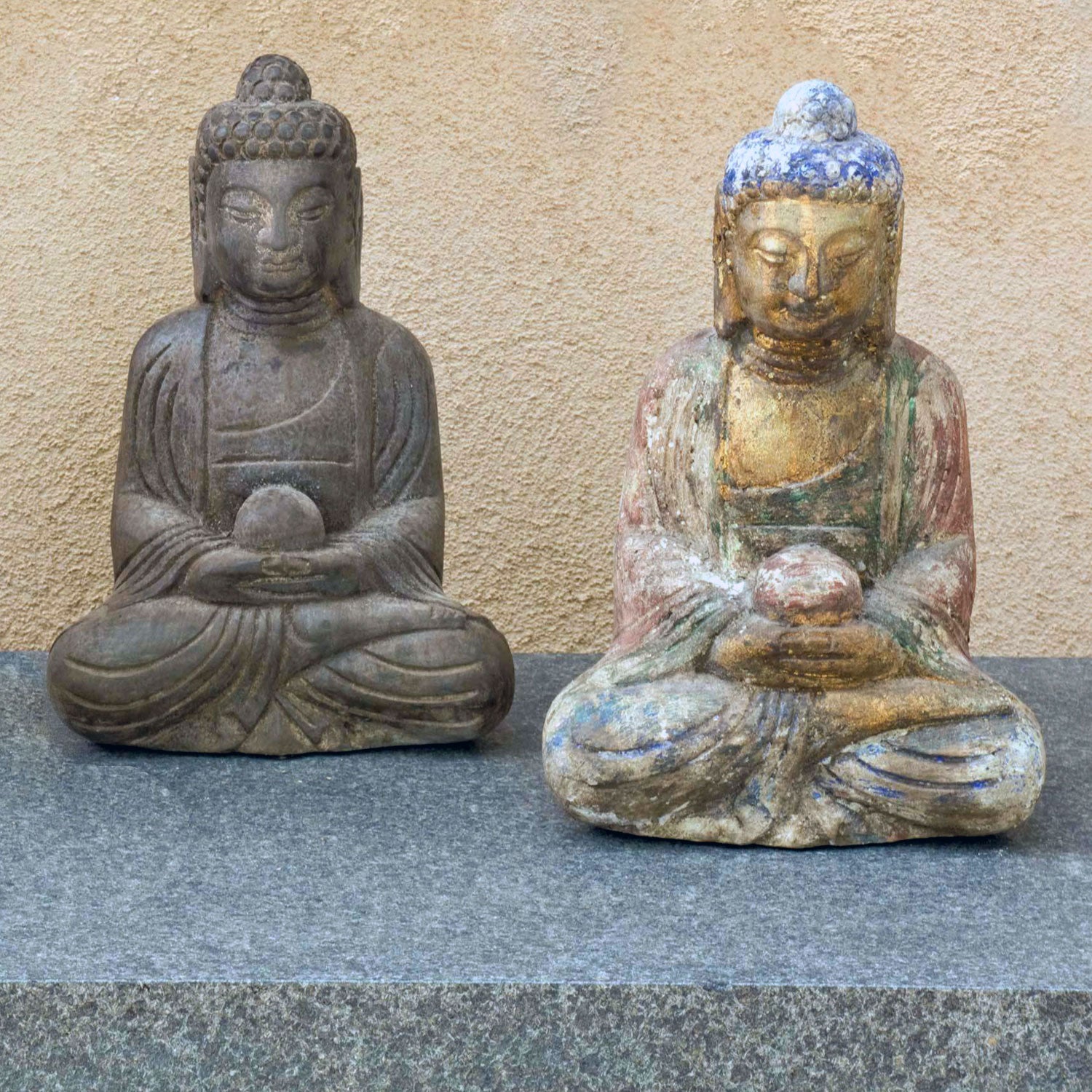Two hand-carved one in dark limestone Buddha statues. One with with a painted finish. Both seated