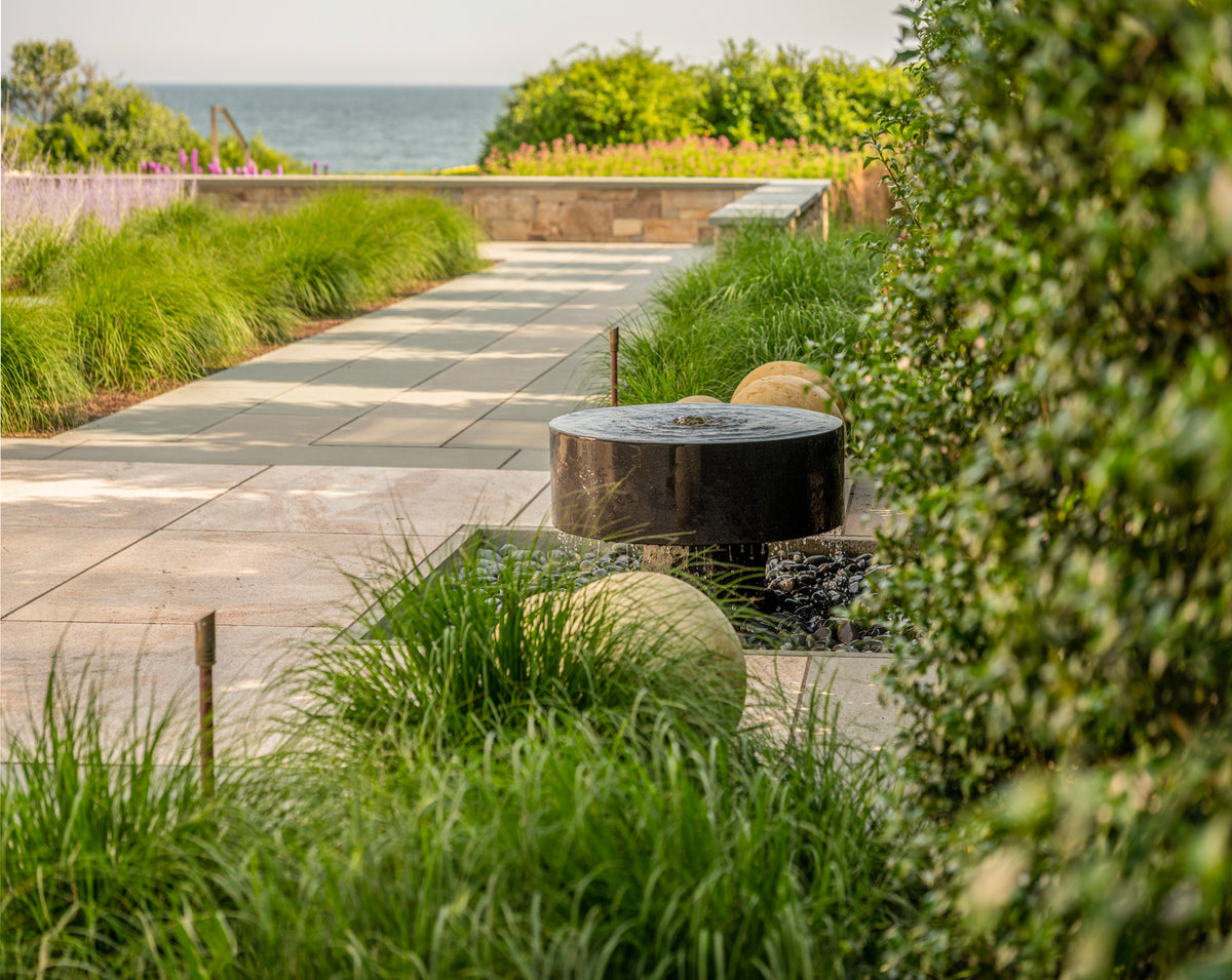 Polished black millstone installed in garden overlooking ocean