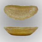 A free-form onyx bowl with a smooth, curved shape in a honey color against a gray background.