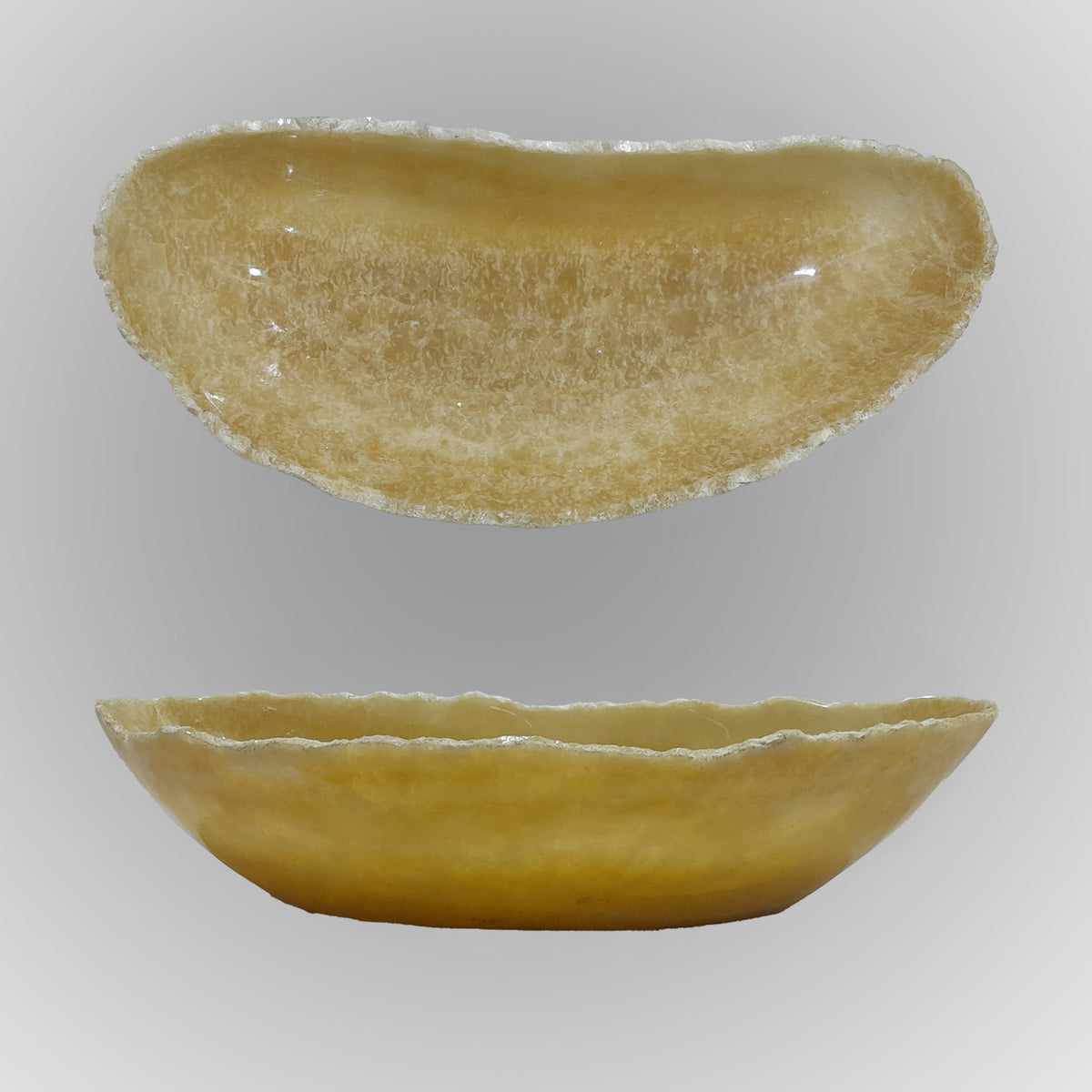 A free-form onyx bowl with a smooth, curved shape in a honey color against a gray background.