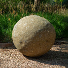 28" stone sphere on a gravel surface with grass and plants in the background