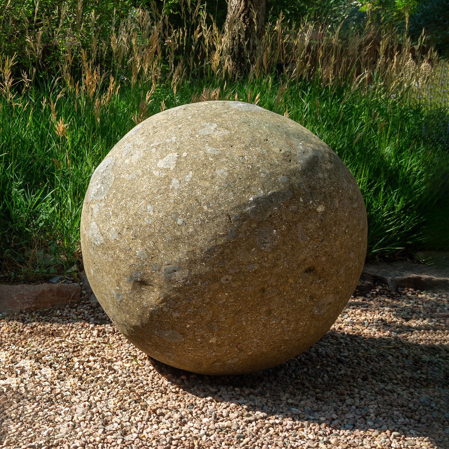 28" stone sphere on a gravel surface with grass and plants in the background