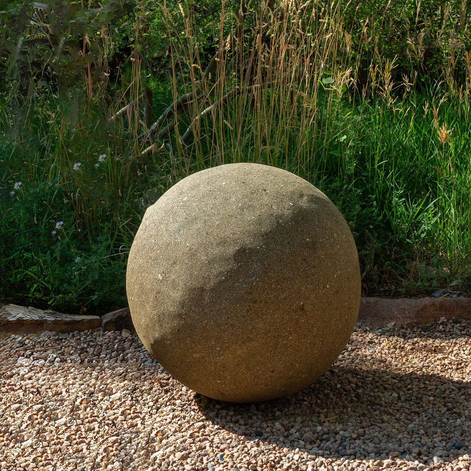 24" stone sphere on a gravel surface with greenery in the background