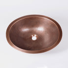 An oval-shaped, hammered copper sink with a patinated finish.