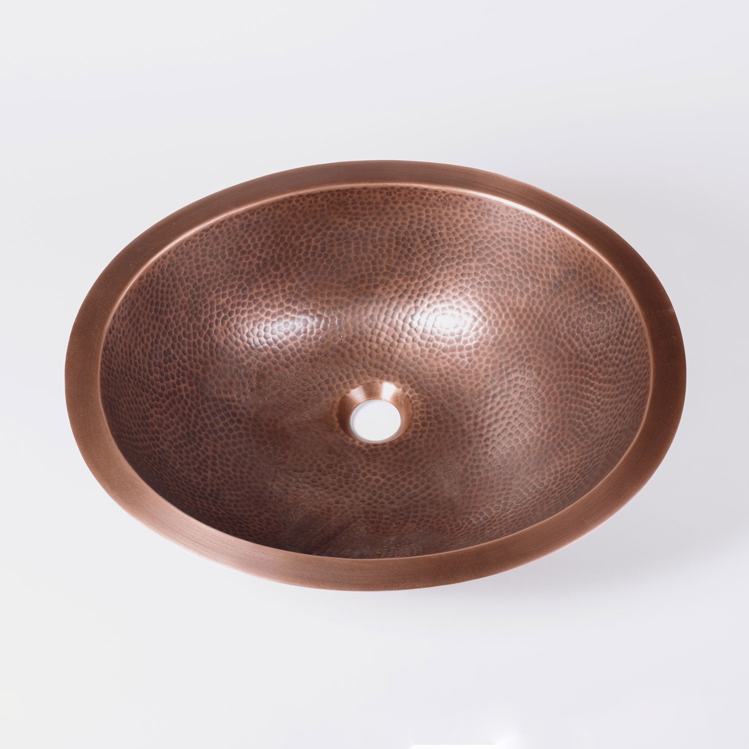 An oval-shaped, hammered copper sink with a patinated finish.