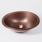 An oval-shaped, hammered copper sink with a patinated finish.