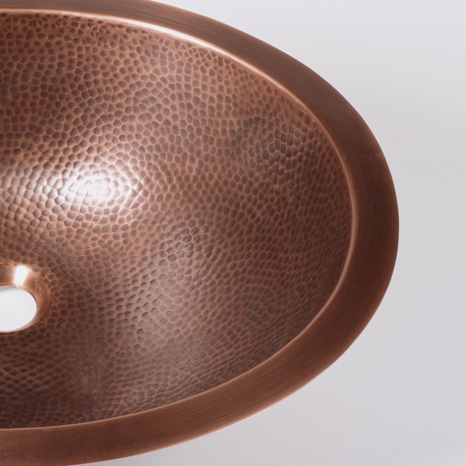 An oval-shaped, hammered copper sink with a patinated finish.
