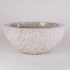 A round vessel sink made of rose granite with a rough, chiseled texture on the exterior and a polished interior and rim.