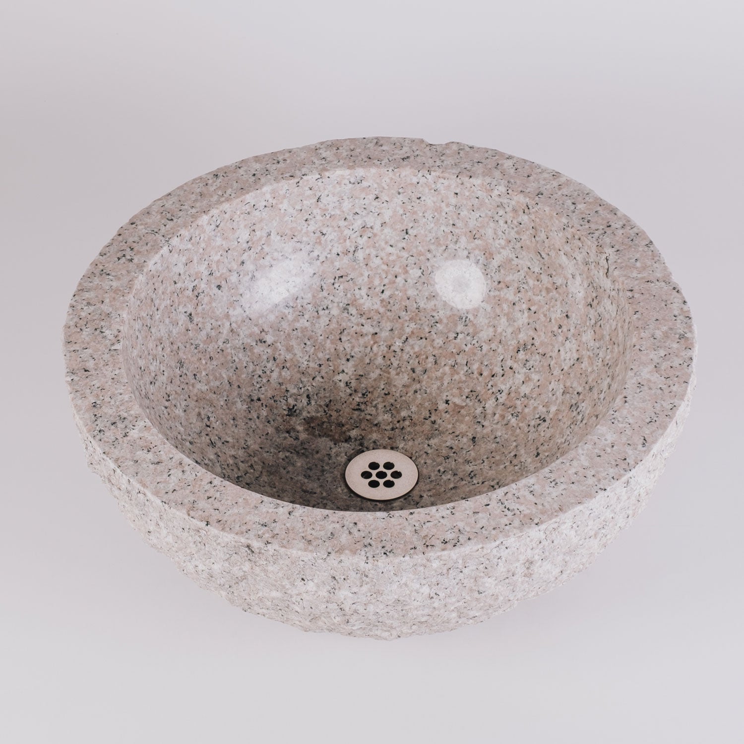 A round vessel sink made of rose granite with a rough, chiseled texture on the exterior and a polished interior and rim.