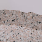 A round vessel sink made of rose granite with a rough, chiseled texture on the exterior and a polished interior and rim. detail