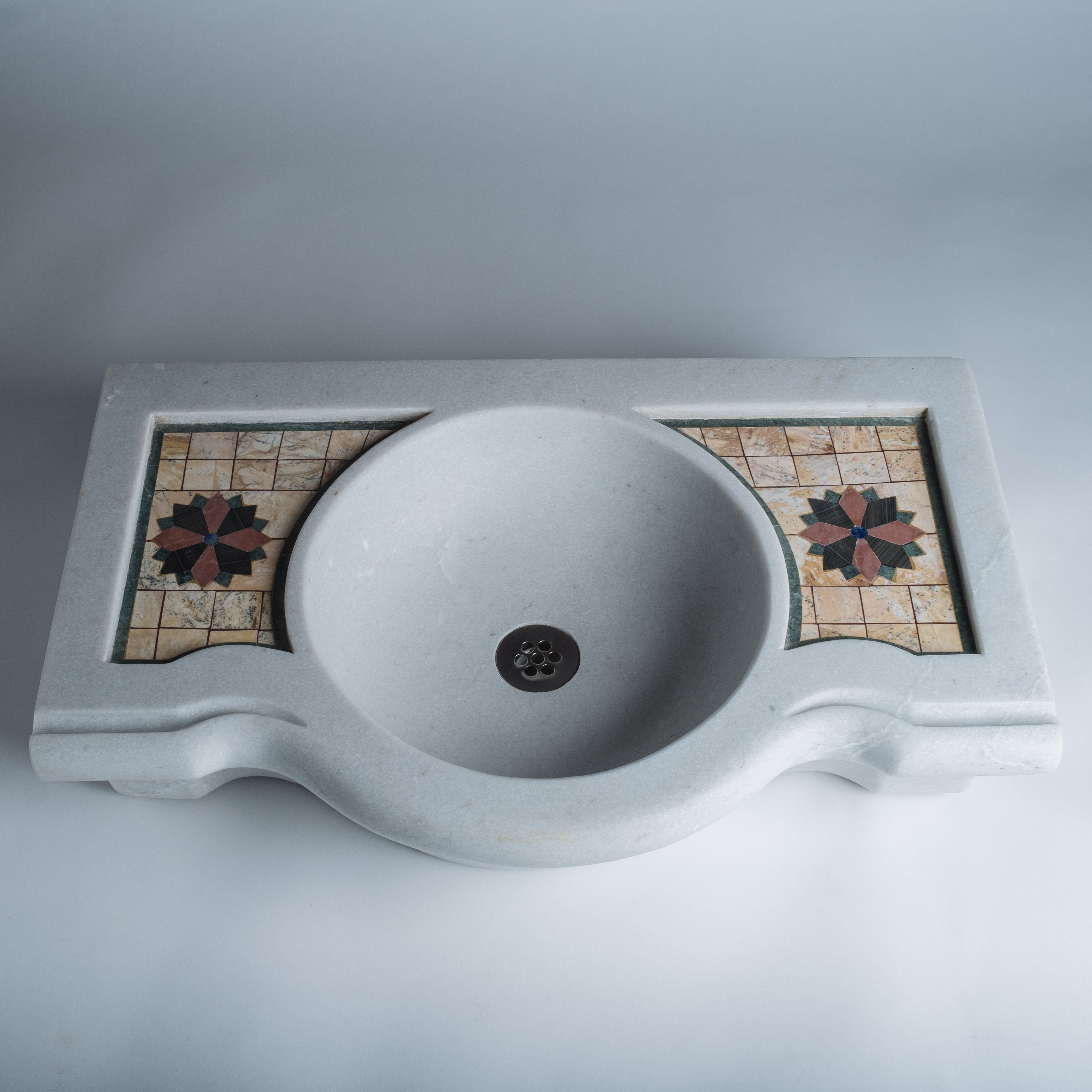 A white marble console sink with a mosaic inlay design on the top surface.