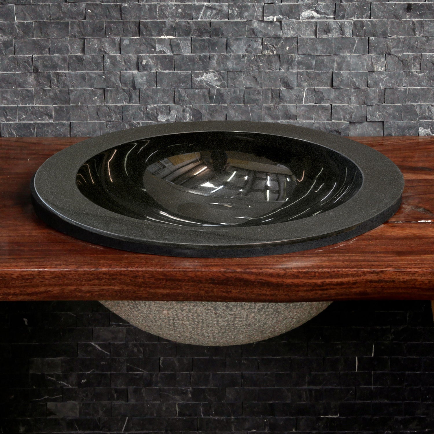 A black granite self-rimming sink placed on an iron stand, with a polished finish and bushed hammer finish on the exterior.
