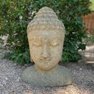 Stone Buddha head sculpture on a gravel surface with greenery in the background