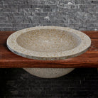 A beige granite self-rimming sink is placed on a wooden countertop with a dark granite backdrop.
