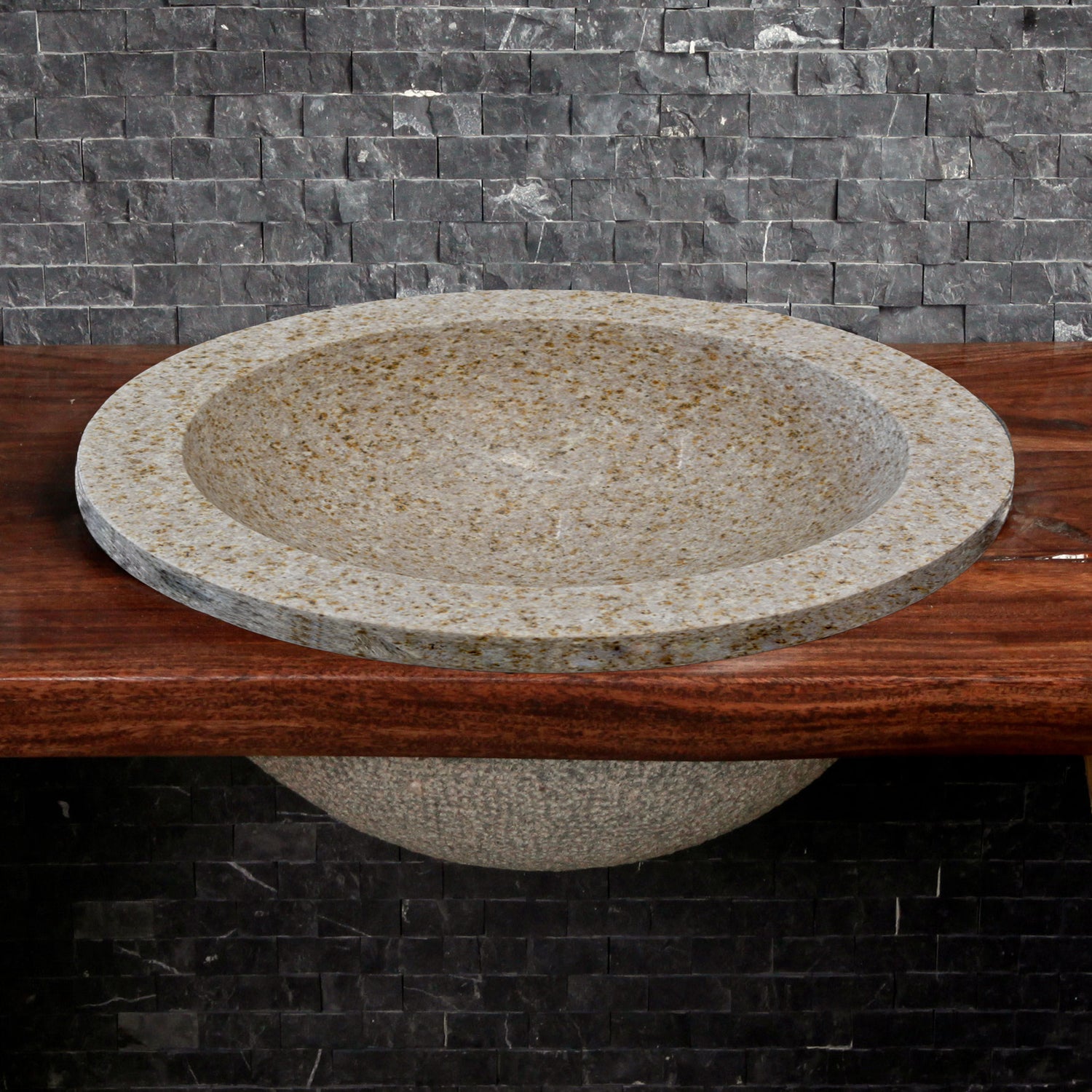 A beige granite self-rimming sink is placed on a wooden countertop with a dark granite backdrop.
