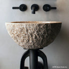 Oval Sink is carved from a block of beige granite with a rough chiseled exterior and polished interior.