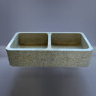 A beige granite double basin farmhouse kitchen sink with a polished interior and a bush hammered apron.