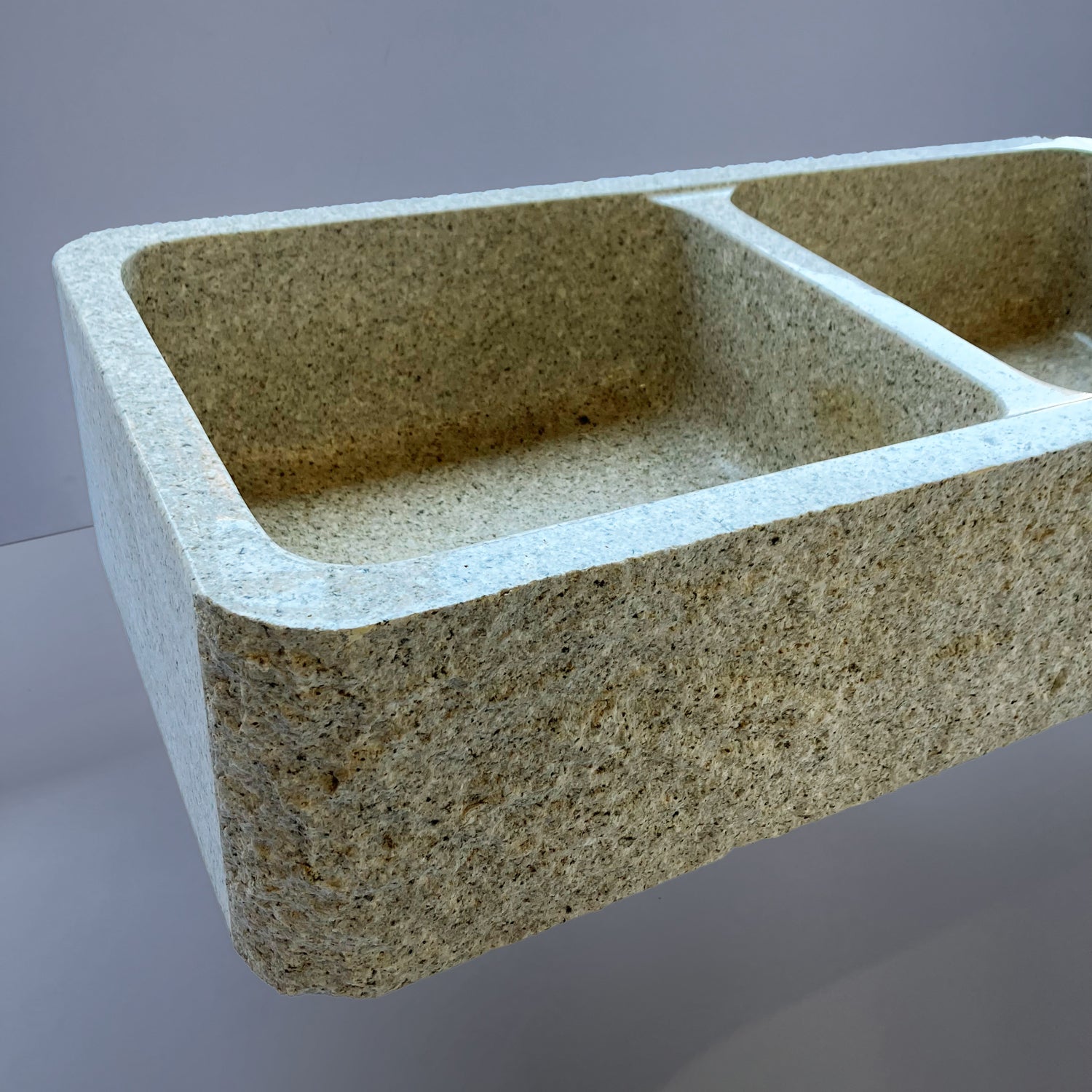 A beige granite double basin farmhouse kitchen sink with a polished interior and a bush hammered apron.