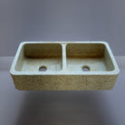 A beige granite double basin farmhouse kitchen sink with a polished interior and a bush hammered apron.