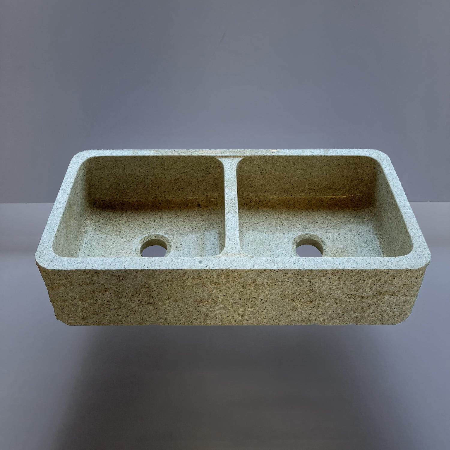 A beige granite double basin farmhouse kitchen sink with a polished interior and a bush hammered apron.