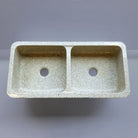 A beige granite double basin farmhouse kitchen sink with a polished interior and a bush hammered apron.